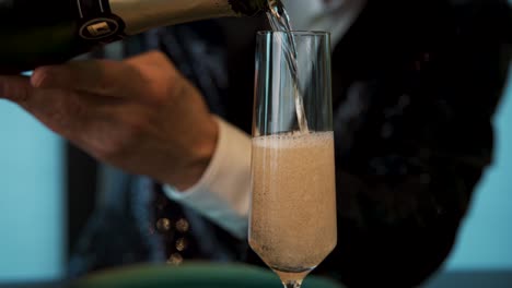 Pouring-champagne-in-tuxedo-with-both-hands-into-tall-glass-at-party