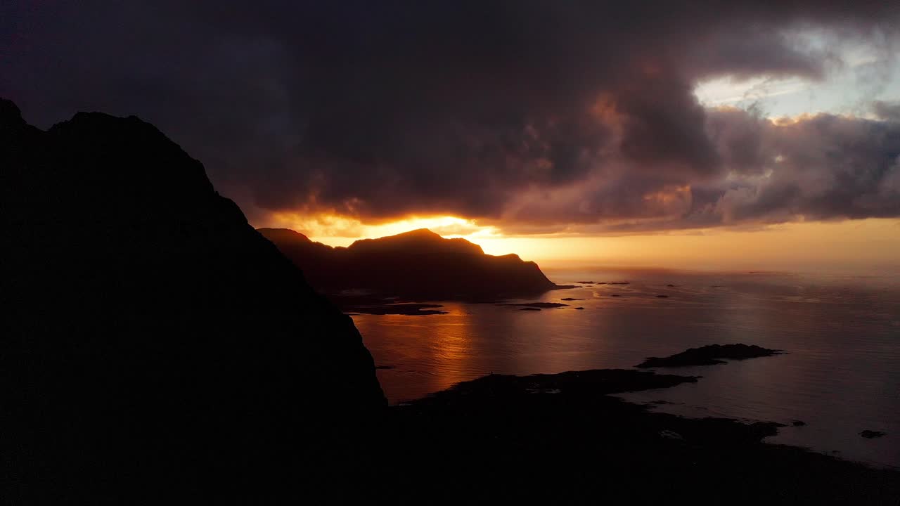 vista aérea, revelando la hermosa puesta de sol detrás de las montañas de flakstad playa de surf, islas lofoten, noruega