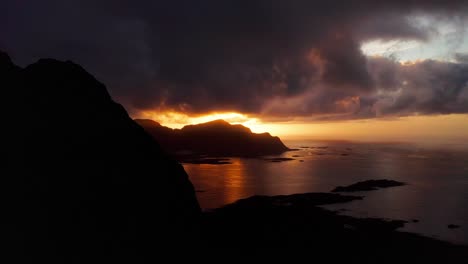 Vista-Aérea,-Que-Revela-La-Hermosa-Puesta-De-Sol-Detrás-De-Las-Montañas-De-La-Playa-De-Surf-Flakstad,-Islas-Lofoten,-Noruega