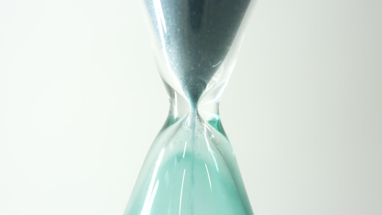slow motion footage of green sand falling through the centre of an hour glass in close up