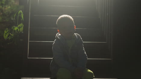 child sitting on cottage stairs silhouette at night. little boy rests alone on steps at country house entrance. abandoned kid waits for parent on pouch