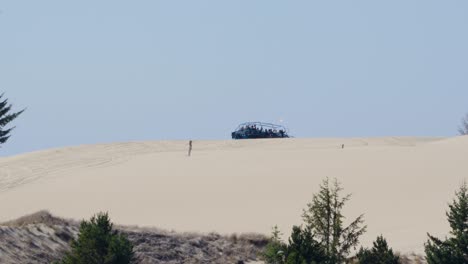 Off-road-buggy-full-of-people-drives-off-behind-the-peak-of-a-white-sand-dune