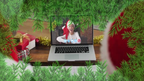 Grüne-Zweige-über-Vater-Und-Sohn-Mit-Weihnachtsmützen,-Die-Während-Der-Weihnachtszeit-Einen-Videoanruf-Auf-Dem-Laptop-Führen