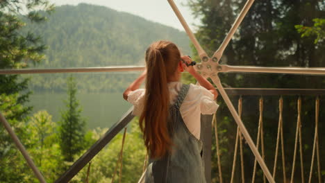 child with camera takes records at glamping. little girl shoots wild landscape with videocamera through glass wall. kid plays on family holiday