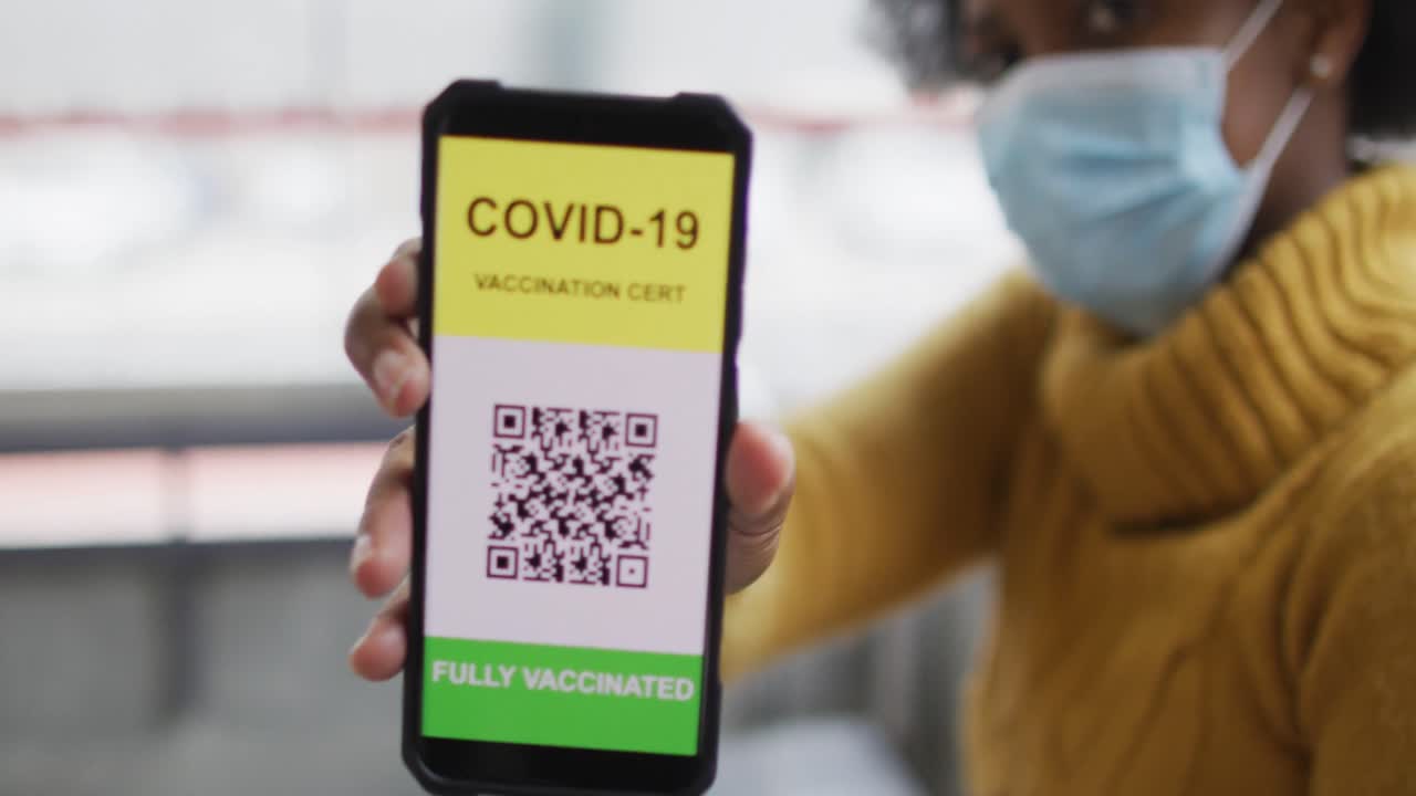 African american businesswoman with face mask preparing covid 19 certification on smartphone