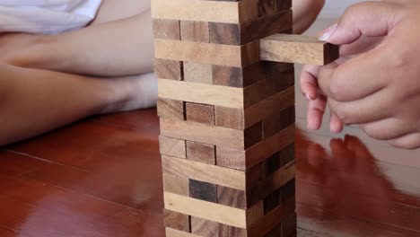 a detailed view of hands carefully extracting a block from a jenga tower on a wooden floor.