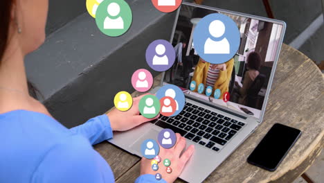 animation of profile icons floating over rear view of woman having a video call on laptop at a cafe