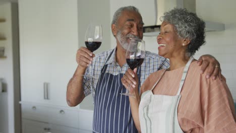 Happy-african-american-senior-couple-drinking-wine-together-in-kitchen