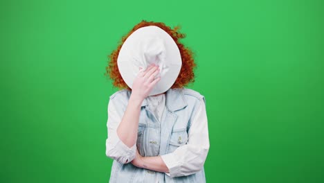 young boring redhead woman rejecting bad idea, rolling up eyes and covering face with panama hat, posing to camera