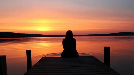 silhouette of a person sitting on a dock at sunset