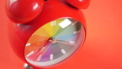 close-up of a red alarm clock with a rainbow face