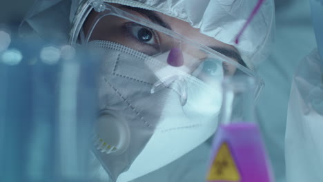 female lab scientist in protective uniform dripping liquid in flask