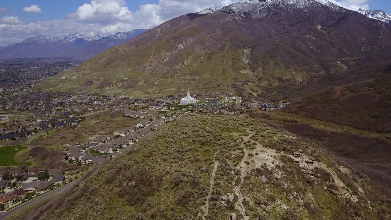 un dron que se eleva disparó sobre una gran colina, revelando el templo lds draper a lo lejos en la base de las montañas wasatch