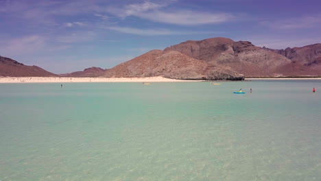 low aerial shot of the sandy balandra beach, paddle boats in the water, baja california sur, mexico