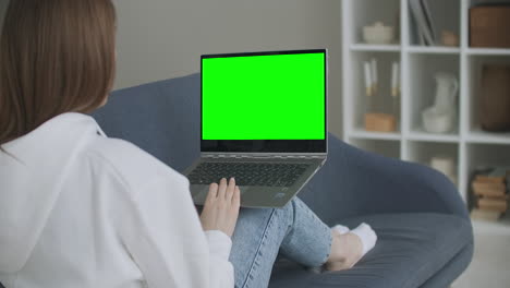 Frau-Zu-Hause-Sitzt-Auf-Einer-Couch-Und-Arbeitet-An-Einem-Laptop-Computer-Mit-Grünem-Mock-up-Bildschirm.-Coronavirus-Covid-19-Quarantäne-Fernunterricht-Oder-Arbeitskonzept.-Mädchen,-Das-Den-Computer-Benutzt-Und-Durchstöbert