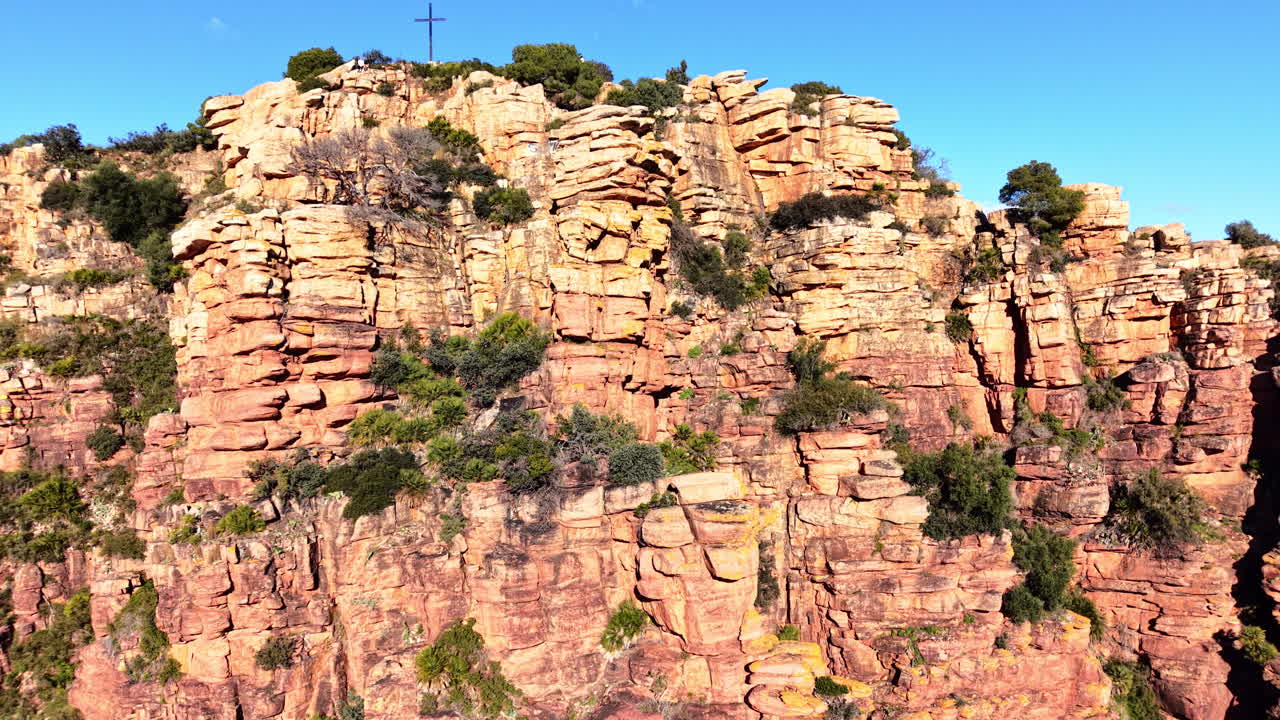 Formazioni rocciose rosse stratificate con cespugli verdi e piccole palme che crescono tra le fessure. Vista aerea ravvicinata della texture di scogliere in arenaria rossa con vegetazione.