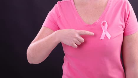 Video-of-midsection-of-caucasian-woman-wearing-pink-cancer-awareness-ribbon,-with-black-background