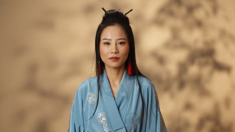 portrait shot of young asian angry woman in blue kimono looking at camera with serious expression and punching with fist