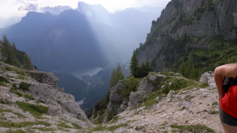 Blonde-female-tourist-in-a-red-shit,-putting-her-phone-away-and-continuing-the-hike-in-a-beautiful-mountain-range-in-Europe