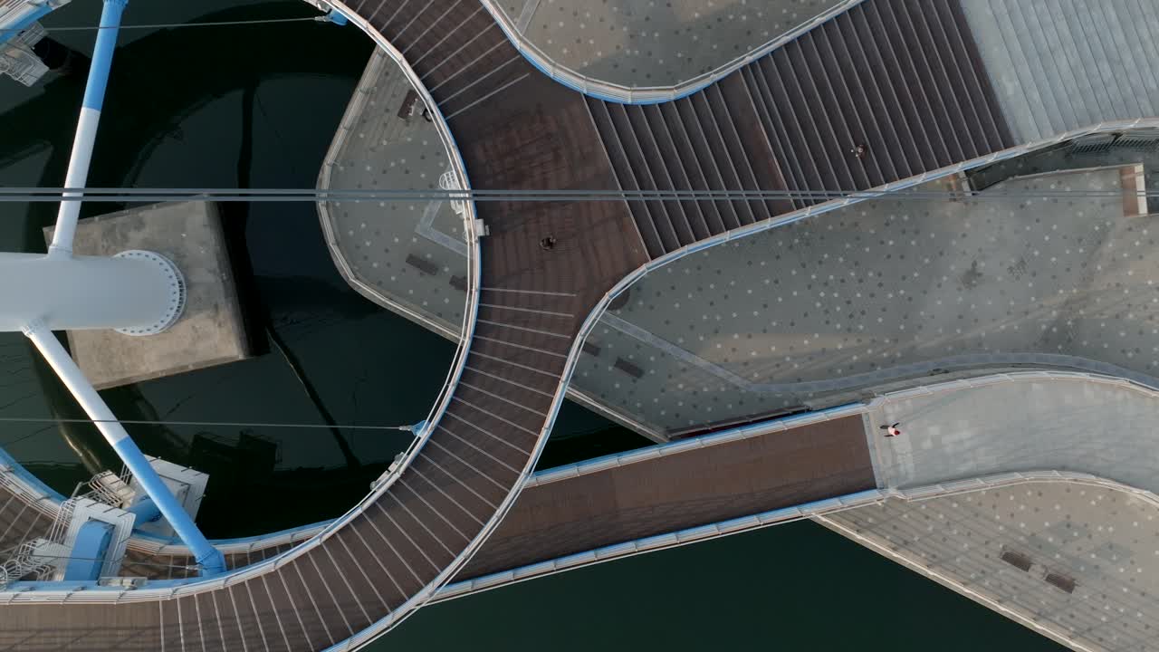 Drone shot showing a person walking over a cable-supported bridge with clear shadow lines in Masan Marine Park.