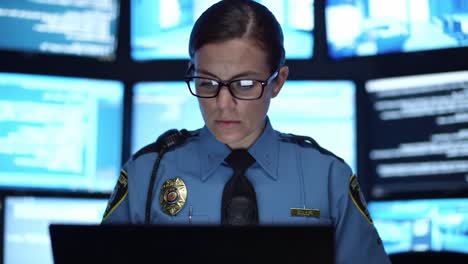 focused female officer analyzing data in high-tech control room surrounded by multiple screens displaying security information