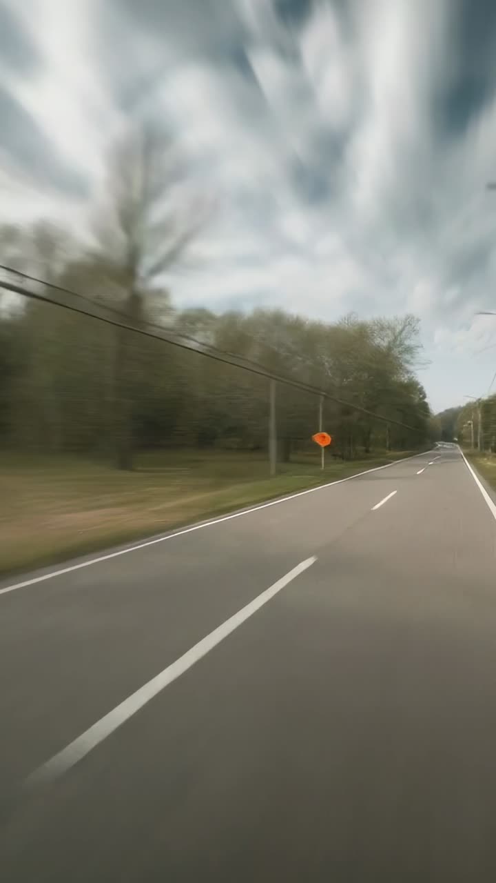 Vertical video: Moving camera capturing two-lane road sliding by rural roadside, with orange sign