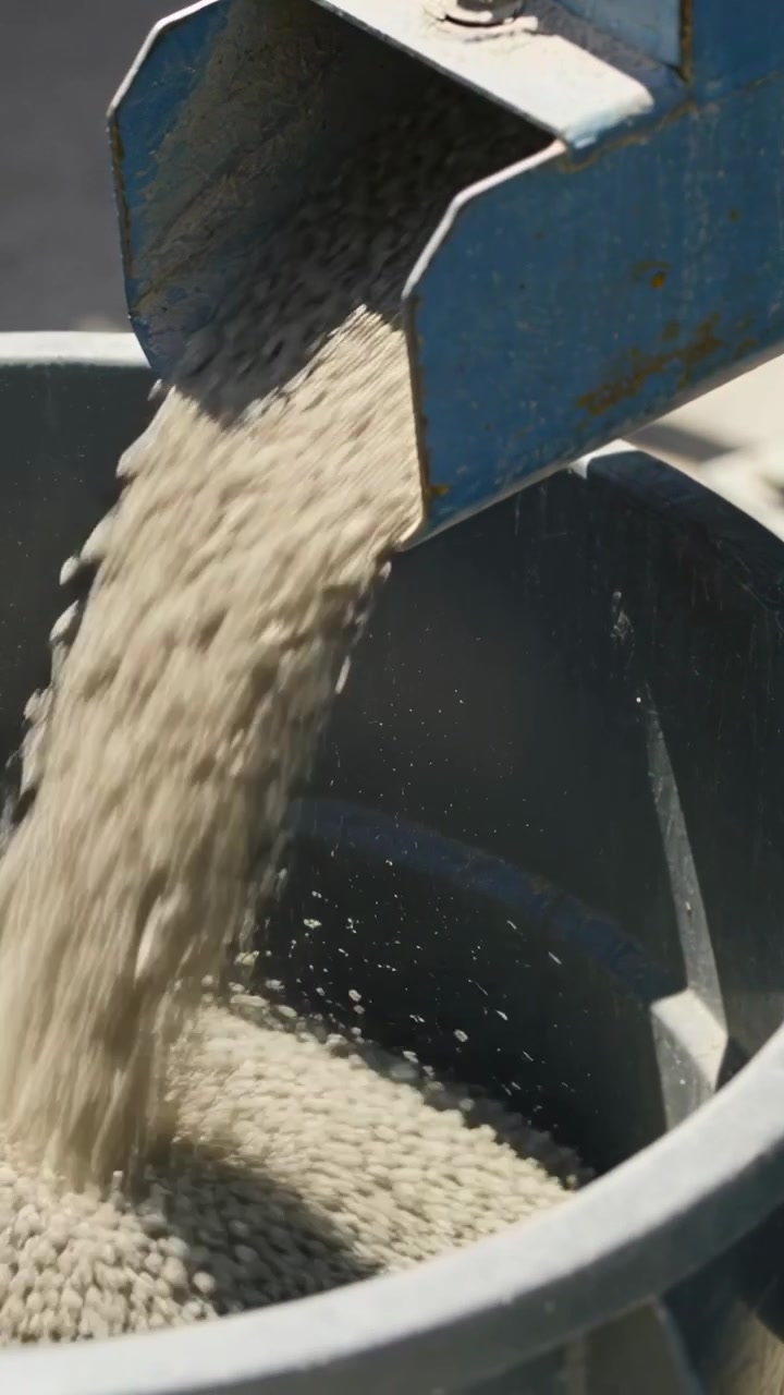 Vertical video: Starting blue chute dumping light granules into drum for pickup at yard, with bolt