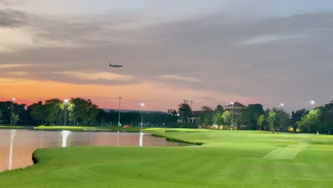 plane flies over golf course during sunset