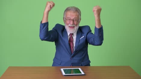 handsome senior bearded businessman against green background