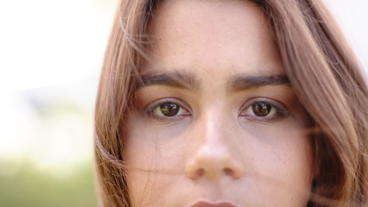 Mulher olhando fixamente para a lente enquanto a brisa movimenta o cabelo, colocando mechas atrás das orelhas para enxergar.