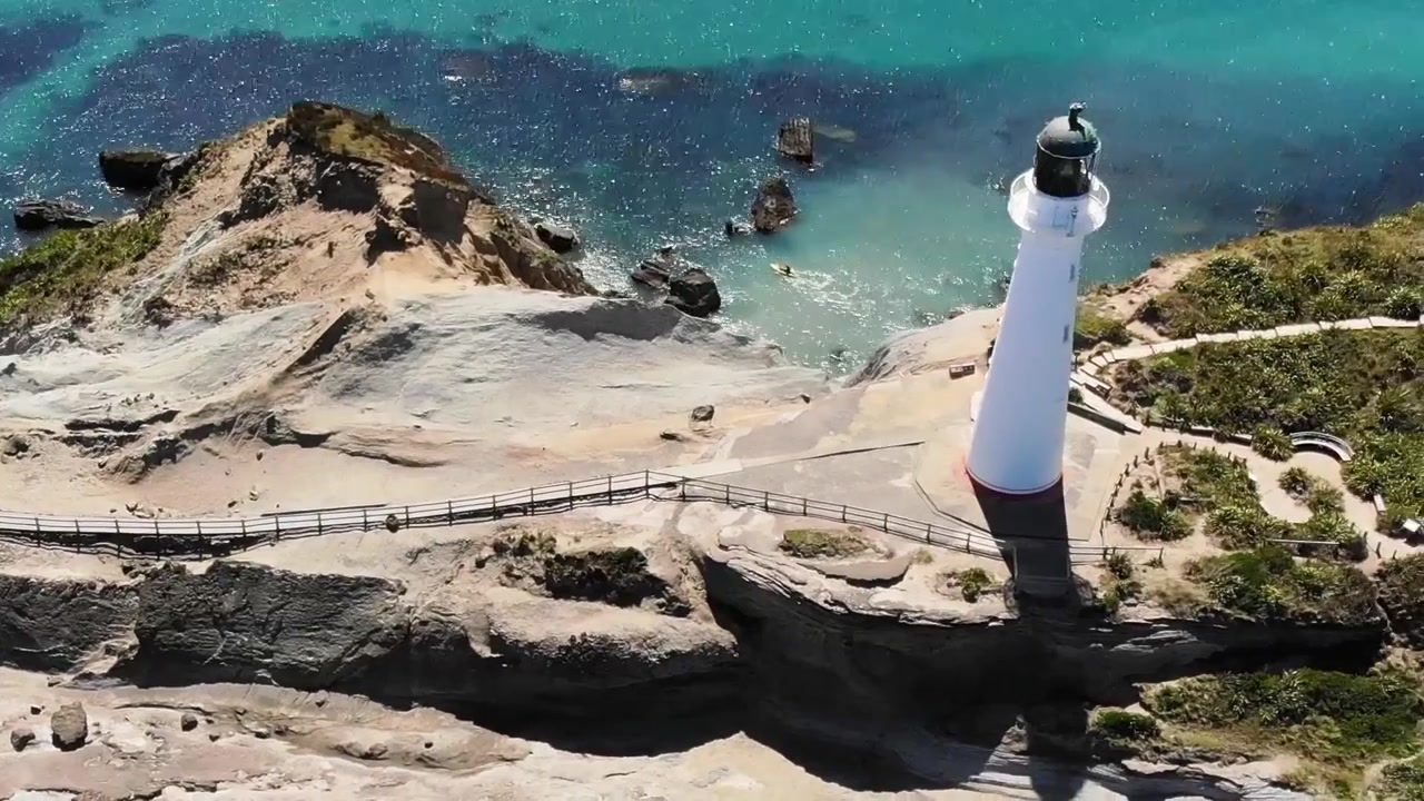 Drone-uitzicht naar beneden op een rotsachtig rif met een loopbrug naar de Castlepoint-vuurtoren, een schilderachtige bezienswaardigheid in Nieuw-Zeeland