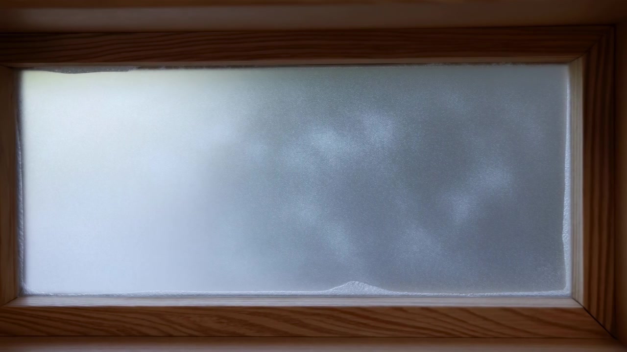 Visto dall'interno, un pannello di vetro smerigliato con una calda cornice di legno riempie il centro della scena. La luce soffusa del giorno attraversa la superficie testurizzata.