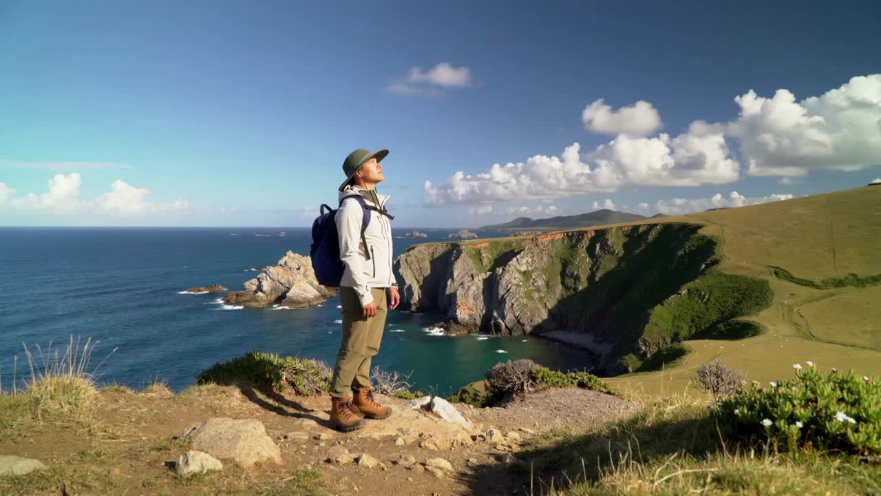 Horizon spotting, escursionista che si sporge verso l'alto su una scogliera in riva al mare con cappello a tesa larga, zaino e scarponi, spazio per il testo