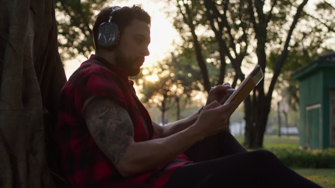 Man drawing on a digital tablet in a park at sunset