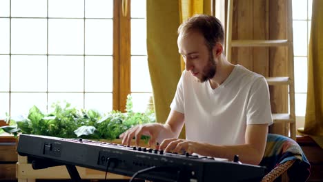 cheerful young man in casual clothes is playing keyboard at home. musical instruments, attractive people, hobby and creativity concept.