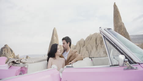 romantic couple in a pink convertible car in the desert