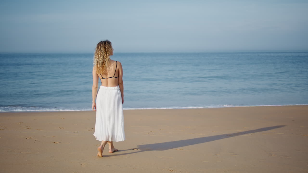 편안한 소녀는 모래 해변을 걸어 저녁 빛에서 휴식을 취합니다.