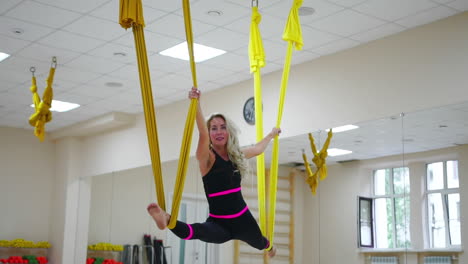 young beautiful yogi woman doing aerial yoga practice in purple hammock in fitness club