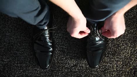 close up of man tying laces on black, shiny dress shoes on dark carpet. inside