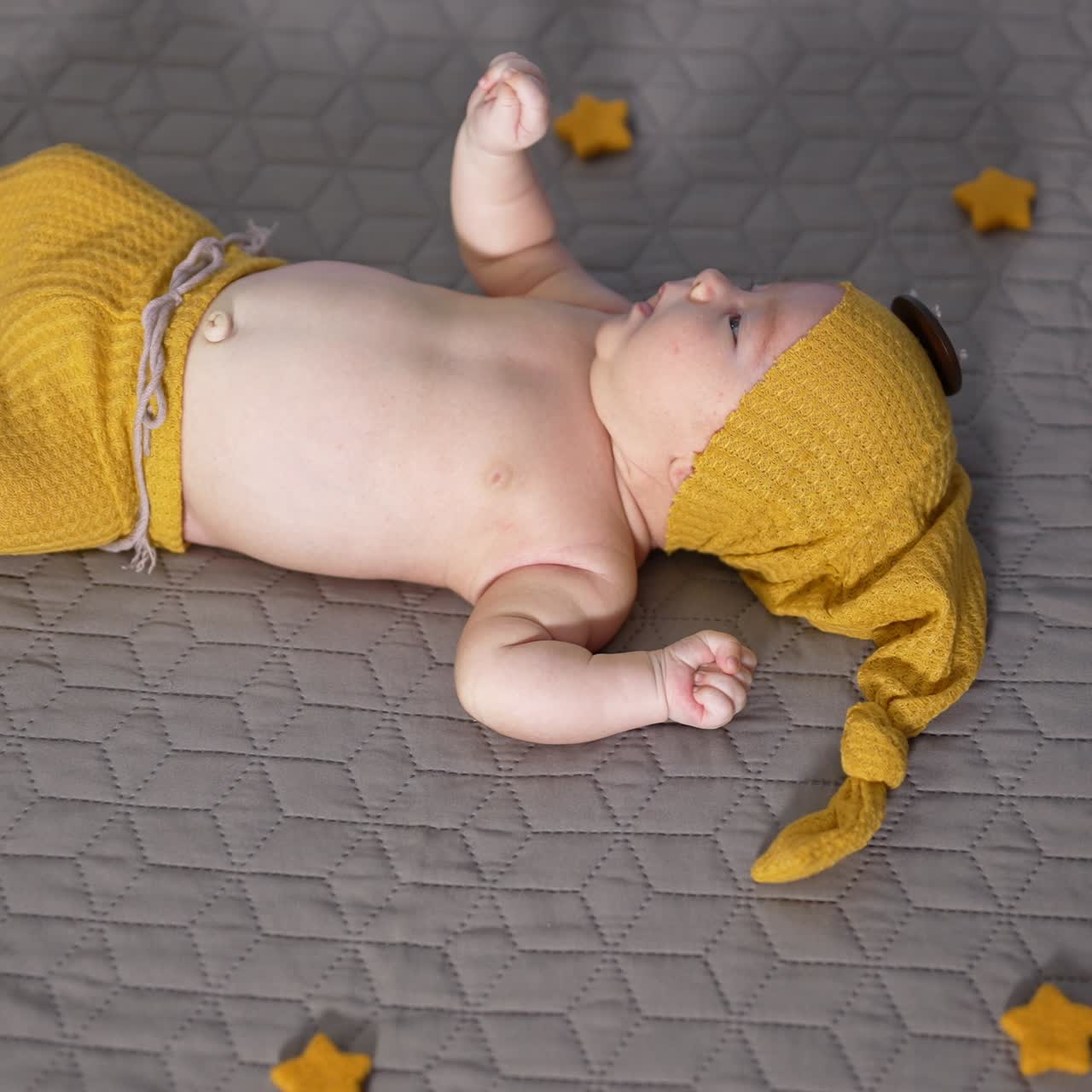 Infant child in a costume of gnome lies on the bed. Sweet boy waving his hands and turns away from the camera. View from above