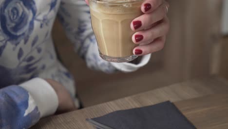 young beautiful girl lifting up flat white coffee, drinking it and taking it back to the table