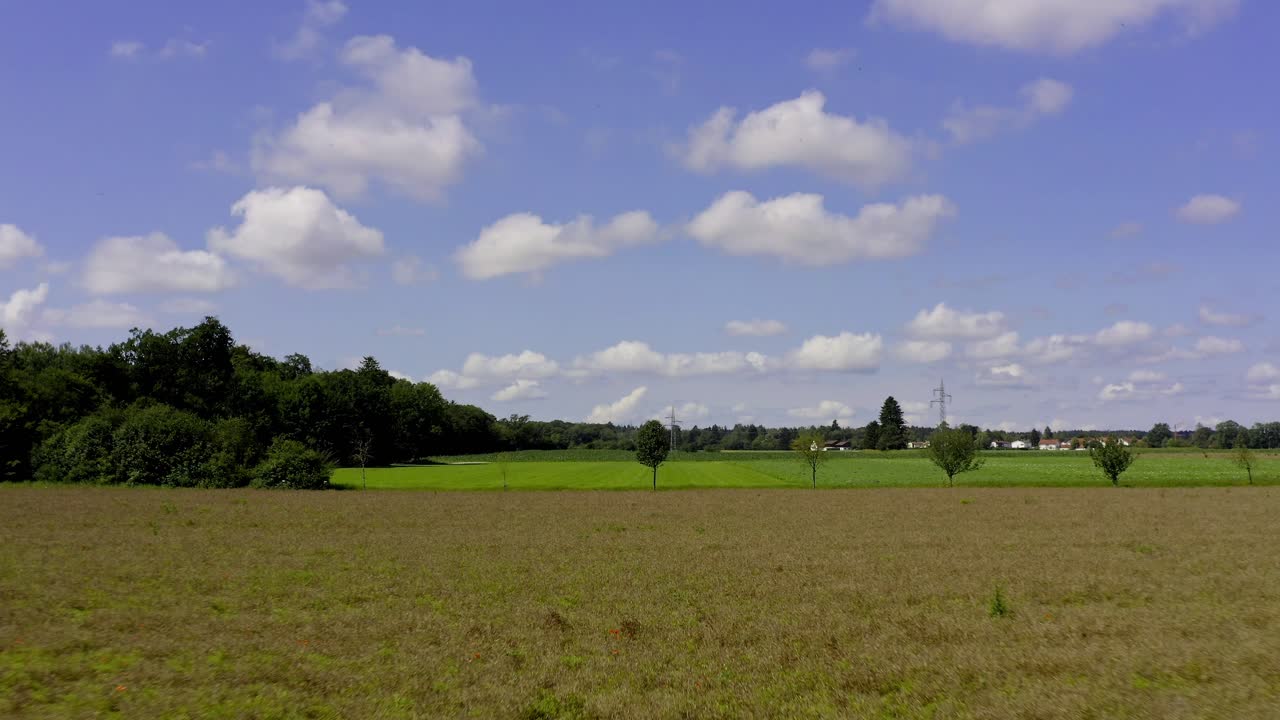 푹신한 흰 구름과 함께 푸른 하늘을 즐기며 여름에 자라는 들판 위를 낮은 높이로 날다