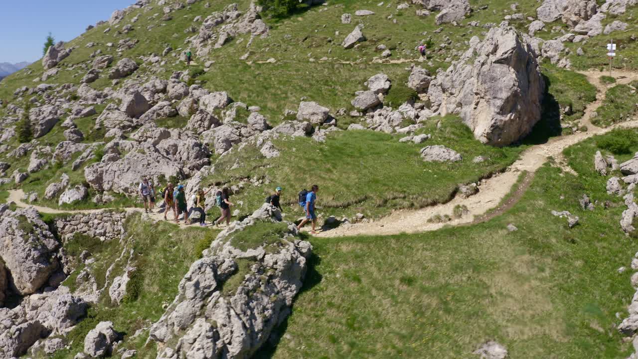Ripresa aerea in tracking di un gruppo di escursionisti che fa trekking su un sentiero di montagna nelle idilliache Dolomiti durante una giornata di sole