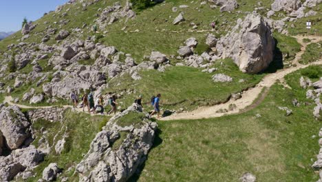 aerial tracking shot of hiker group trekking on mountain path in idyllic dolomites during sunny day