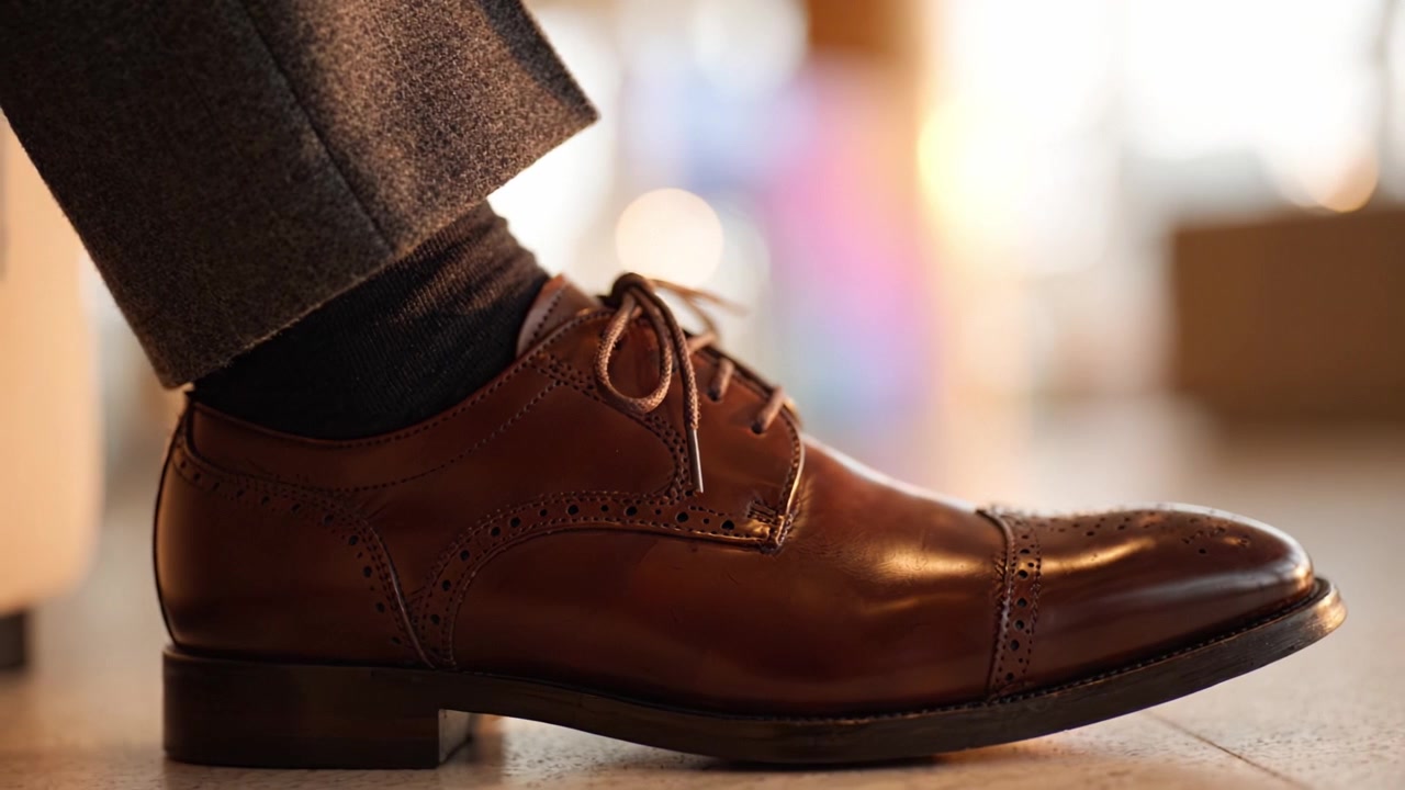 Sepatu Kulit Cokelat Elegan pada Kaki Berpakaian Rapi yang Ditangkap dalam Fokus Lembut, Menampilkan Gaya Klasik dan Perhatian terhadap Detail untuk Aksesori Canggih