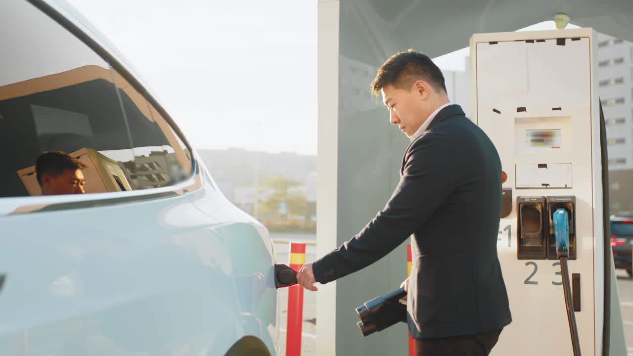 사업가 가 충전소 에서 전기 차량 을 충전 하고 있다