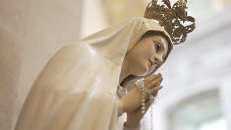 Statue-of-the-Virgin-Mary-with-a-crown,-holding-rosary-beads,-in-a-prayerful-pose