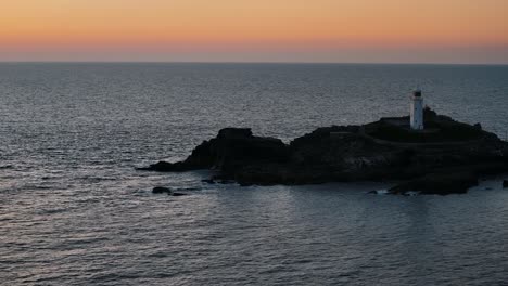 drone dollies right past godfrey’s point lighthouse silhouette at dusk with calm water and glowing sky, panoramic tracking right