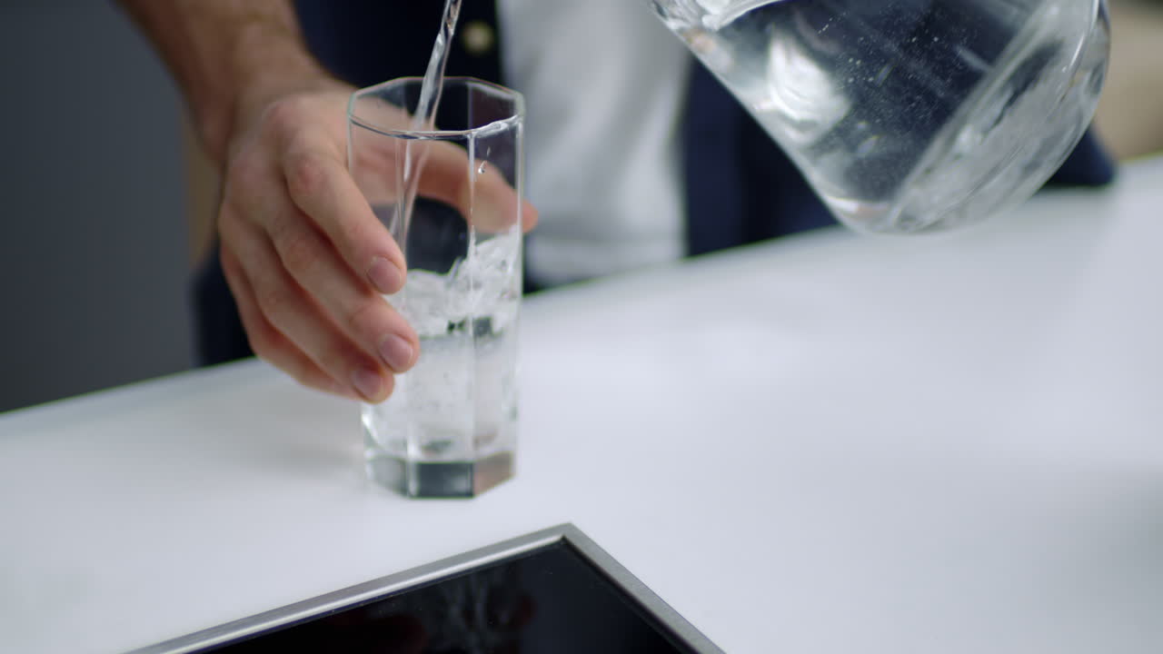 hombre guapo bebiendo agua en la cocina de la casa. manos masculinas vertiendo agua en el vaso