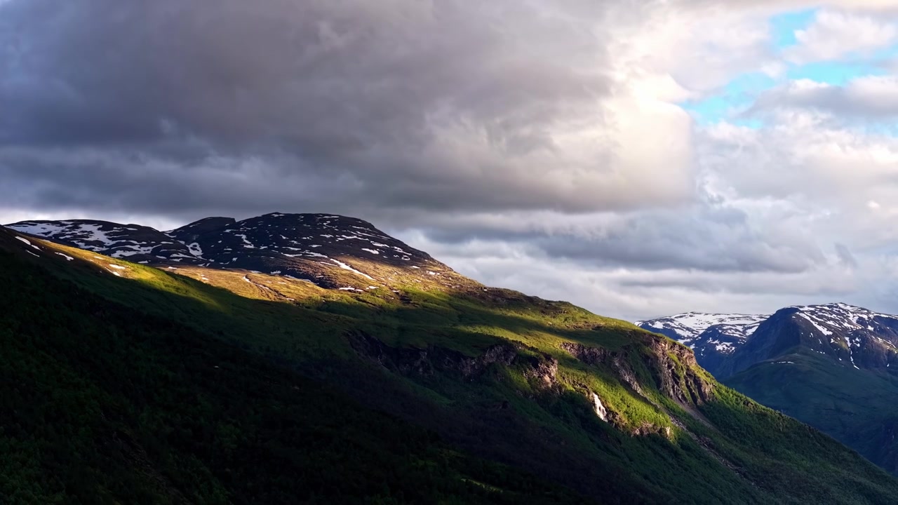 Skyggeskyer beveger seg over grønne fjellsider under dramatiske himler i Norge